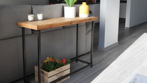 A modern living room with a grey sofa, a wooden console table with a potted plant, a candle, and a small plant box.