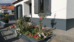 A modern house with a garden in front, featuring a stone pathway and a flower bed with pink and white flowers.