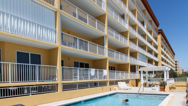 Un hotel con piscina, varios balcones y un cielo azul despejado.