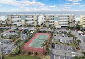 A hotel with multiple floors, a parking lot, and a tennis court. - Gulf Dunes 603 - Coastal Coolness (Fort Walton Beach)