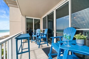 Een balkon met blauwe stoelen en tafels, met uitzicht op een strand.
