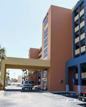Ein Hotel mit großem Parkplatz, überdachter Zufahrt und einem Mehrstöckgebäude mit Balkonen.