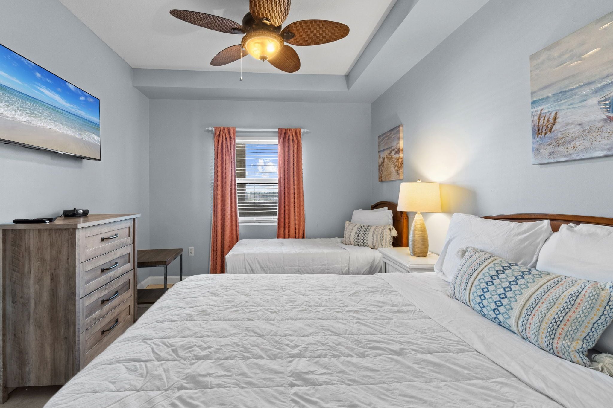 Habitación de hotel con cama, escritorio, cómoda, ventilador de techo y ventana con cortinas.