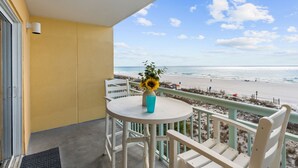Een balkon met een witte tafel en stoelen, een vaas met een zonnebloem en uitzicht op het strand.