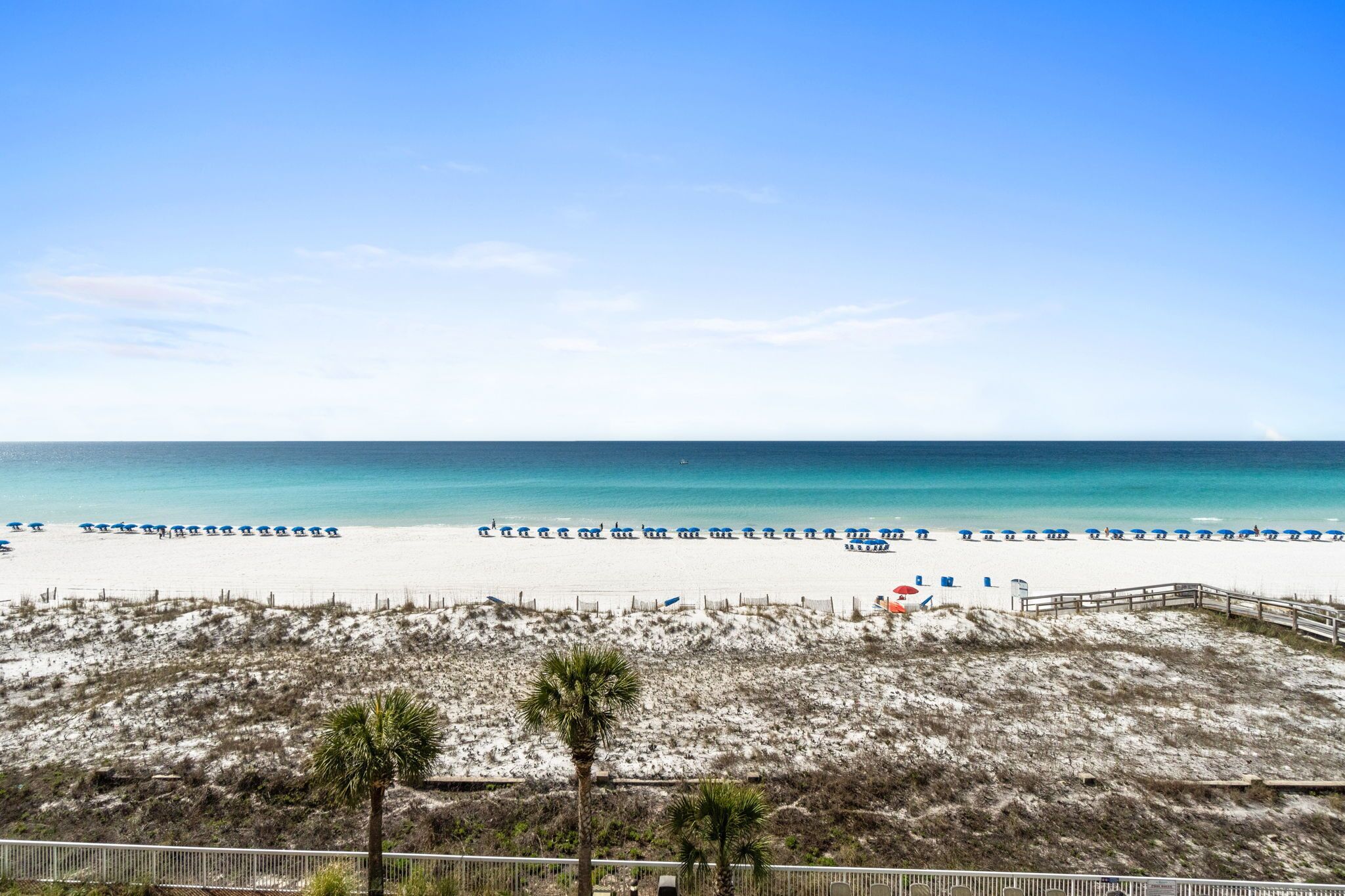 A beach with a wooden walkway, beach umbrellas, and a clear blue sky.