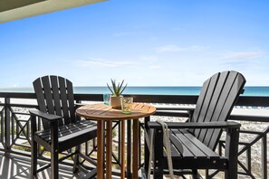 A wooden deck with two Adirondack chairs and a small round table with a potted plant and glass. - Azure 504 - Tranquil Tides (Fort Walton Beach)