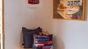 A corner room with a wooden ceiling, a small shelf with a doll, a stack of books, and two framed pictures on the wall. - Mimi's Bunkroom - just outside of Big Bend Nt'l Park (Terlingua)