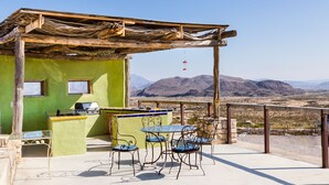 An outdoor patio with a table and chairs, a grill, and a view of mountains. - Mimi's Bunkroom - just outside of Big Bend Nt'l Park (Terlingua)