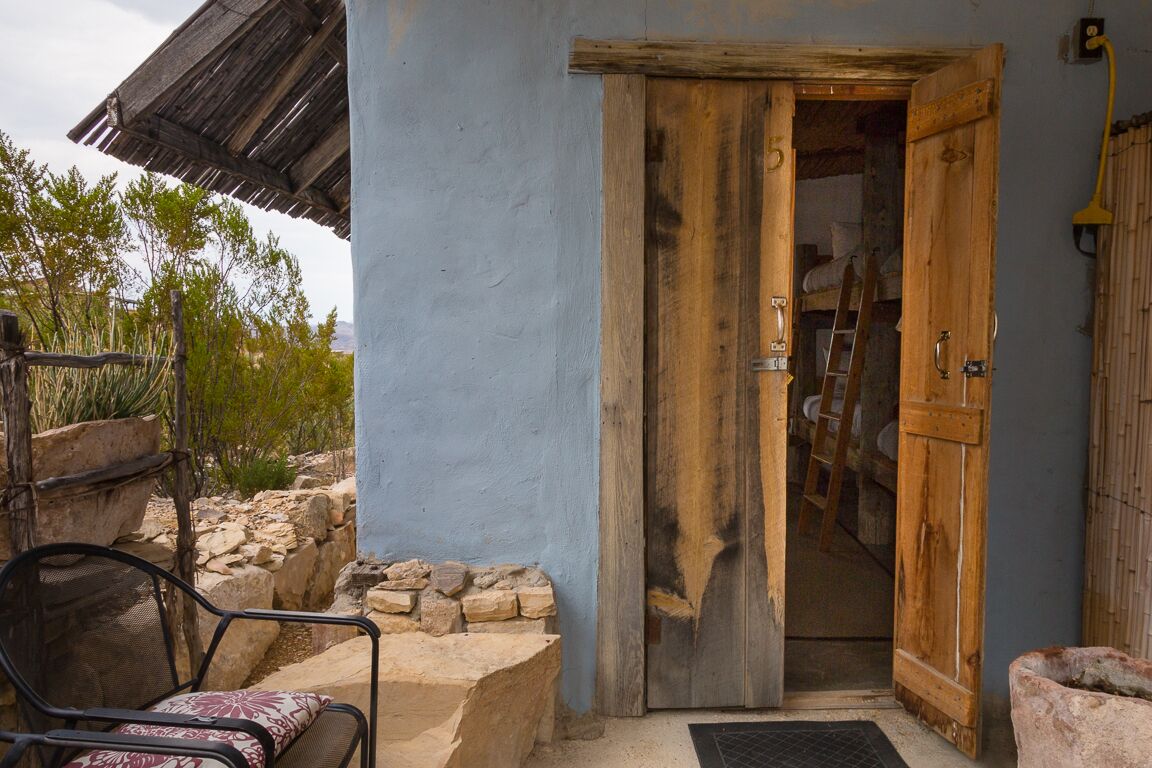 An open wooden door leading into a room with a ladder and a bed.