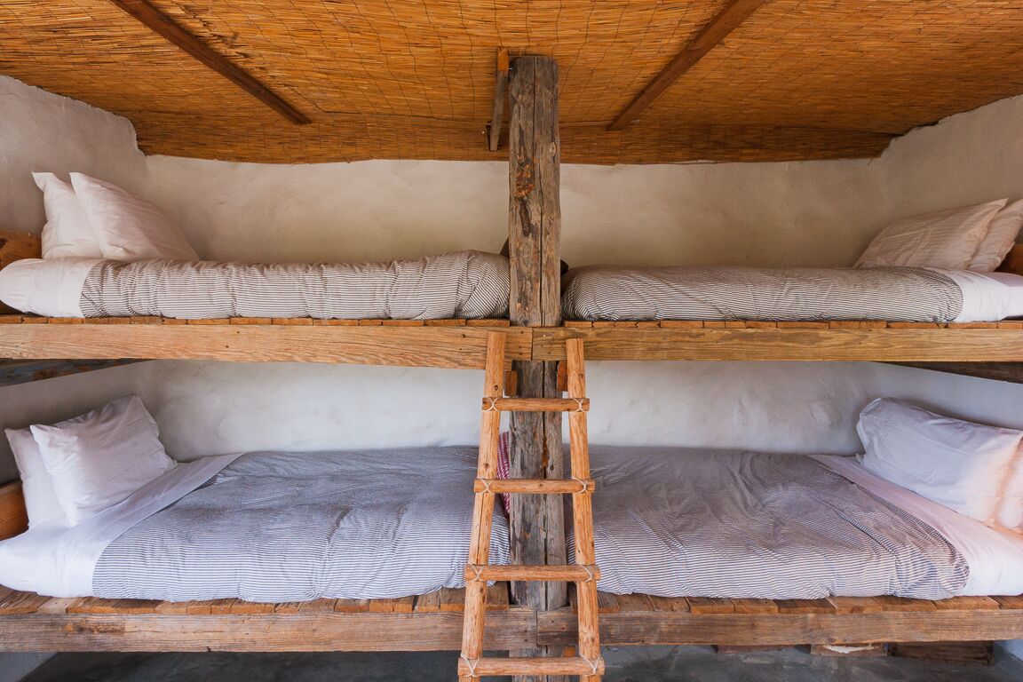 A bunk bed with a wooden ladder in the center, wooden beams on the ceiling, and white bedding.