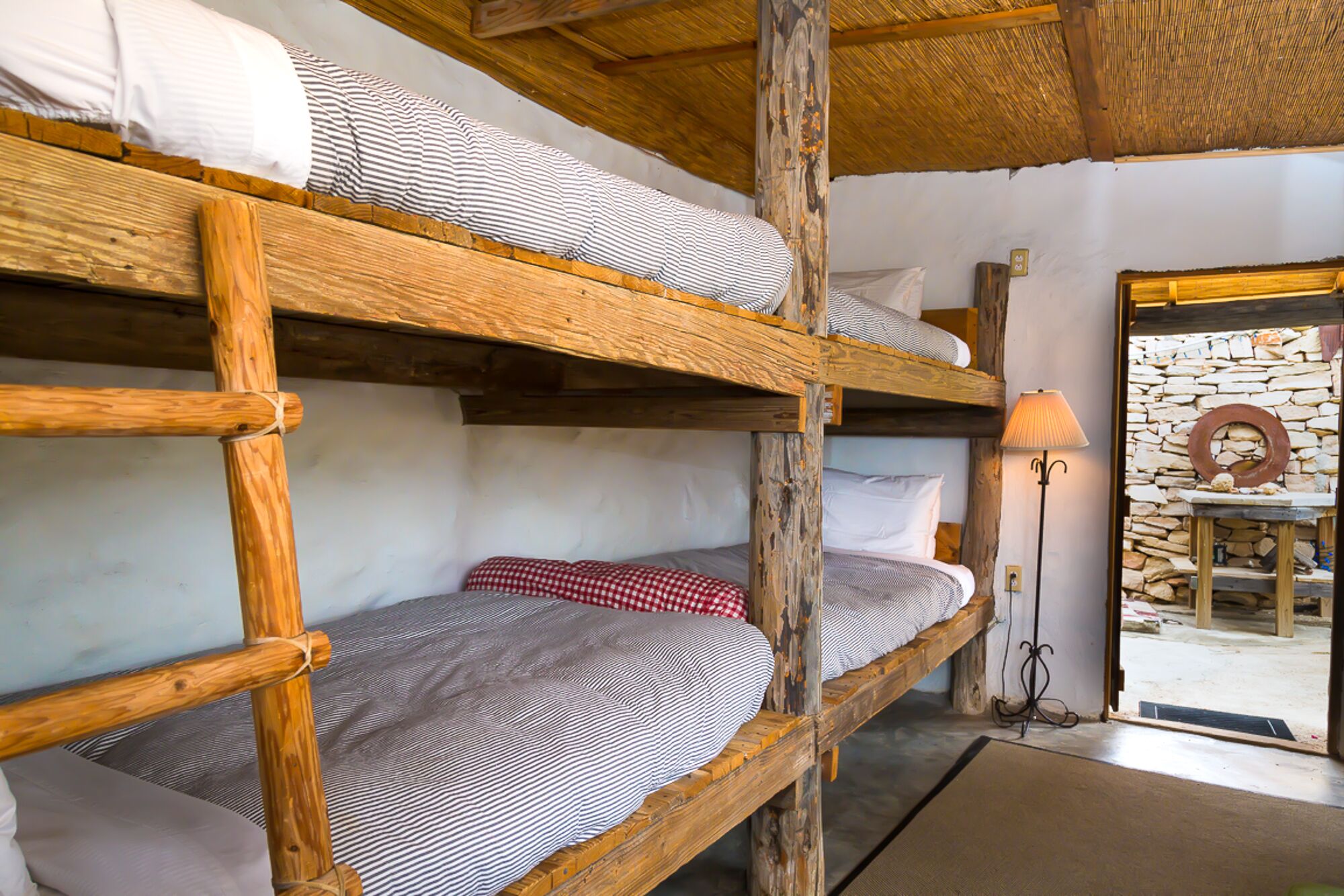 Een slaapkamer met een stapelbed, houten balken, een stenen muur en een lamp.