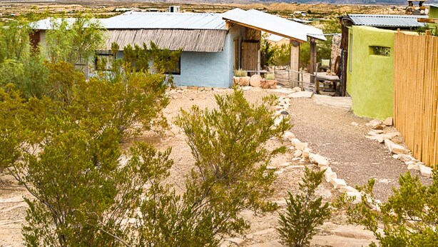 A rural area with several small buildings, including a house with a corrugated metal roof and a green building with a flat roof. - Mimi's Bunkroom - just outside of Big Bend Nt'l Park (Terlingua)
