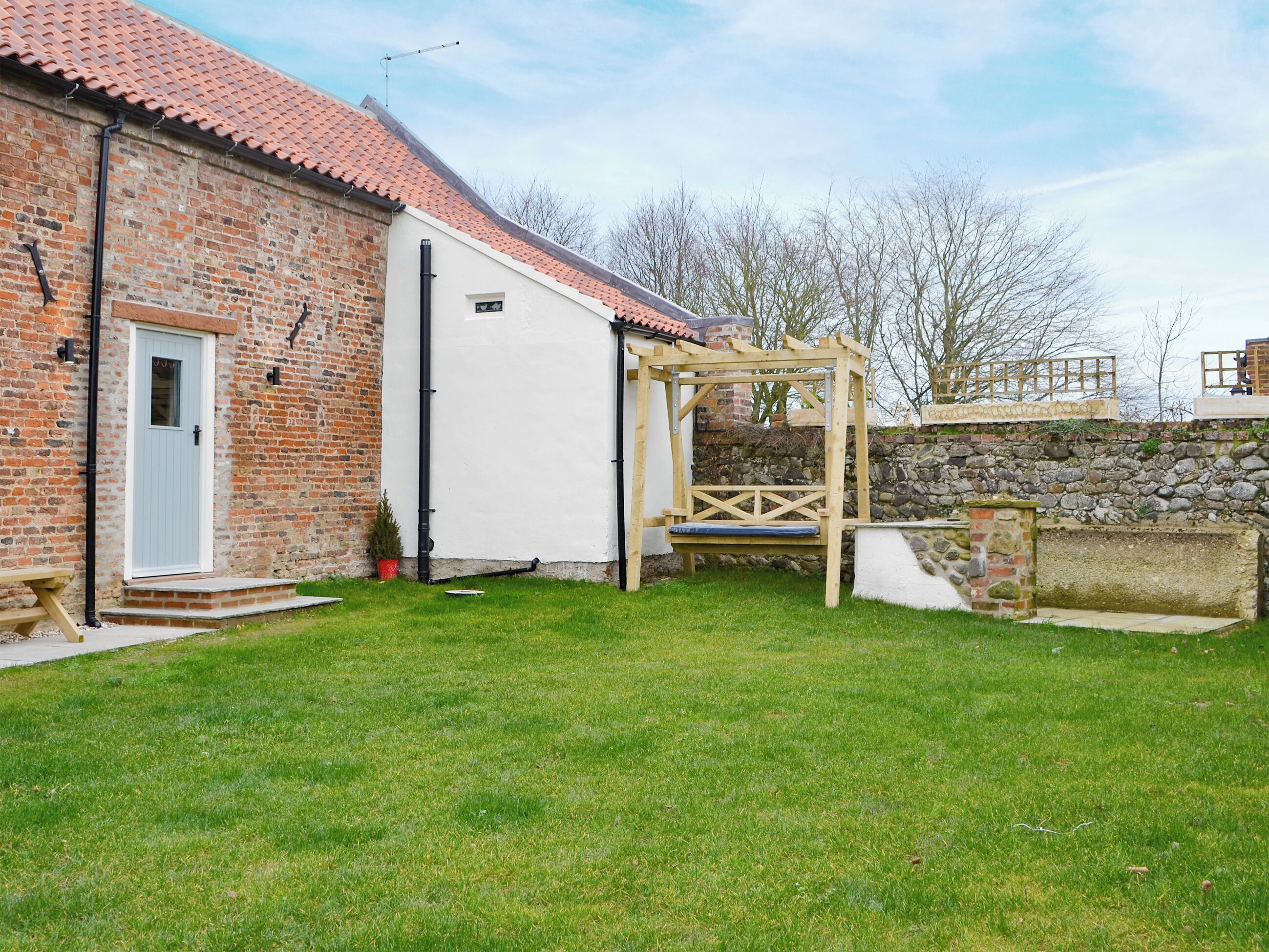 A brick building with a white door, a wooden swing set, and a stone wall.