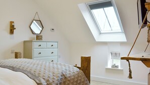 A bedroom with a sloped ceiling, a bed, a dresser, a mirror, a thermostat, a window, and a wooden shelf with a rope swing. - 4 bedroom accommodation in Driffield, near Bridlington (Driffield, near Bridlington)