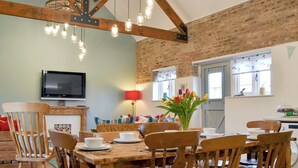 A rustic dining area with exposed wooden beams, a brick wall, and a television mounted on the wall. - 4 bedroom accommodation in Driffield, near Bridlington (Driffield, near Bridlington)