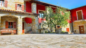 A courtyard with stone flooring, a wooden bench, and a building with red and yellow walls and stone pillars. - Apartament "Pomigranaj"  for 4 person (Marezige)