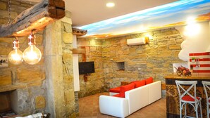 A stone-walled room with a white sofa, red cushions, and a wooden bar area with a television and decorative items. - Apartament "Pomigranaj"  for 4 person (Marezige)