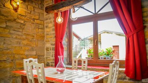 A stone-walled room with a wooden table and chairs, red curtains, and a view of a garden through a window. - Apartament "Pomigranaj"  for 4 person (Marezige)