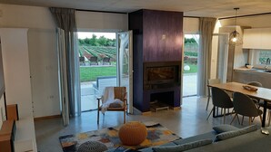 Een moderne woonkamer met een open haard, een eethoek en uitzicht op een tuin.