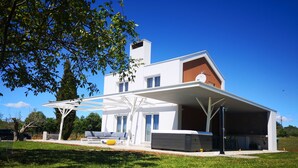 Een modern huis met een overdekt terras, een groot raam en een zichtbaar zitgedeelte buiten.
