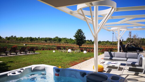 Een hottubgedeelte met een pergola, zitplaatsen buiten en uitzicht op een wijngaard.
