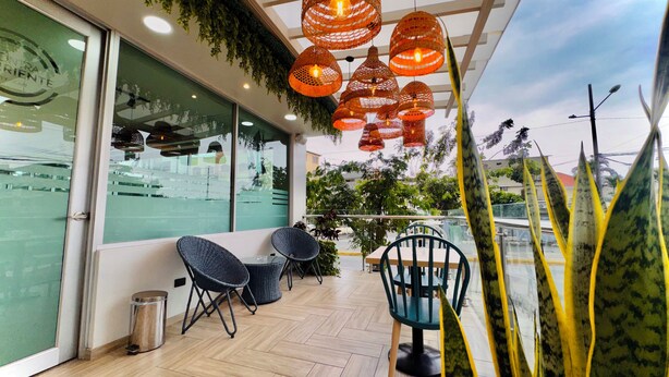 An outdoor seating area with wicker chairs and a table, a glass wall with a reflection, and hanging orange lights. - Hotel Puerto Pacifico Guayaquil Airport (Guayaquil)