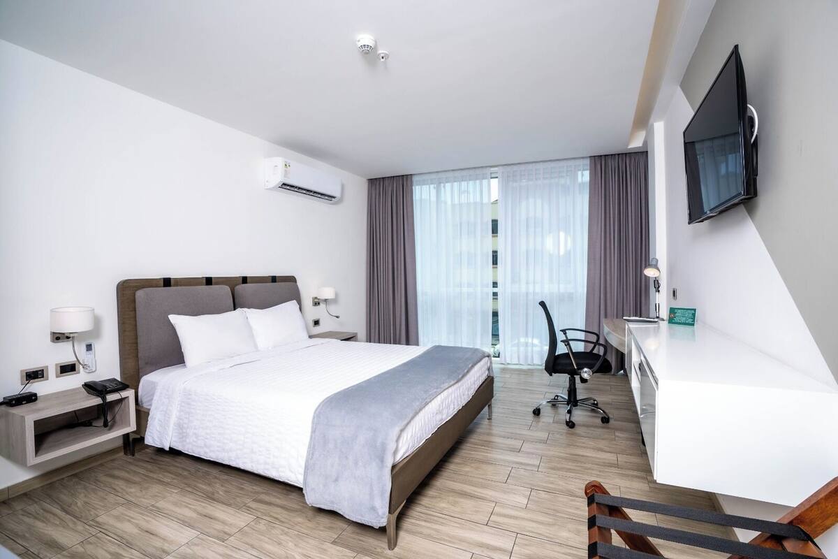 Habitació d'hotel amb llit, escriptori, cadira i televisió.