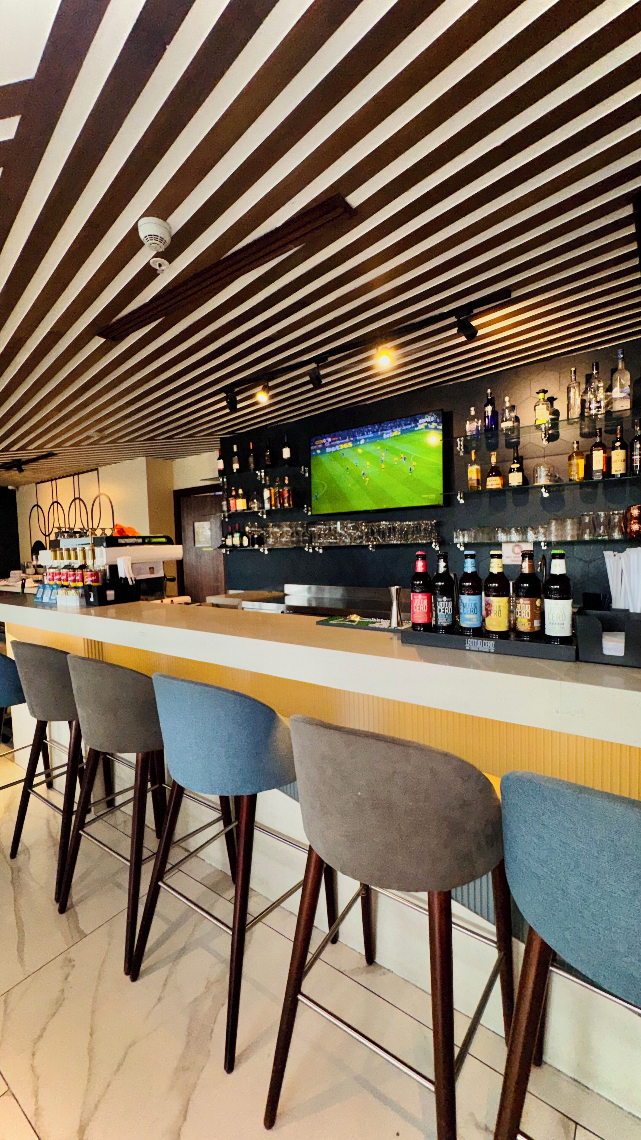 Zona de bar amb un taulell llarg, diverses banquettes i un televisor, a més d'una varietat de garrafes als prestatges.