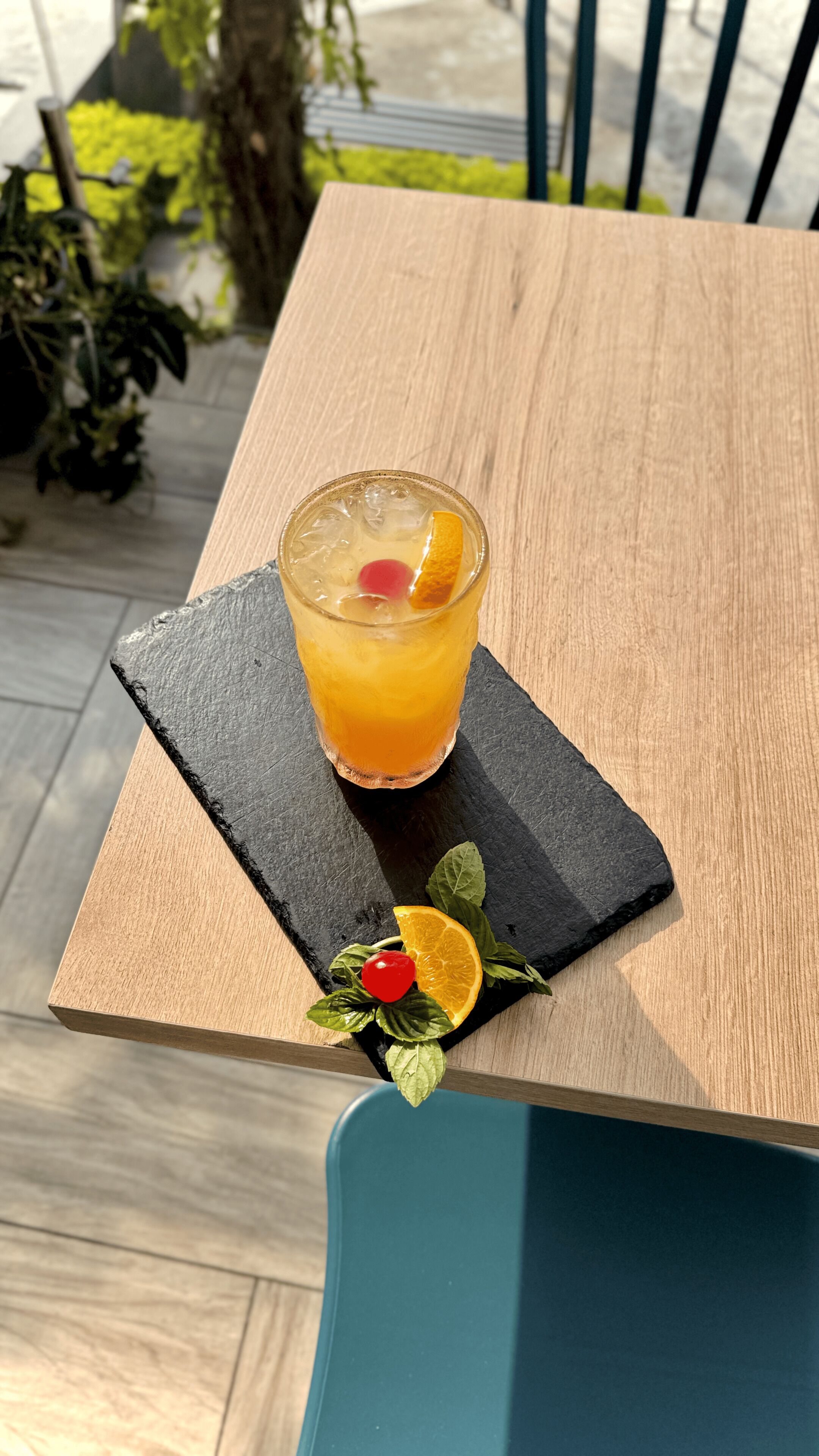 Een glas sinaasappelsap met een kers op een zwarte leisteen onderzetter op een houten tafel.