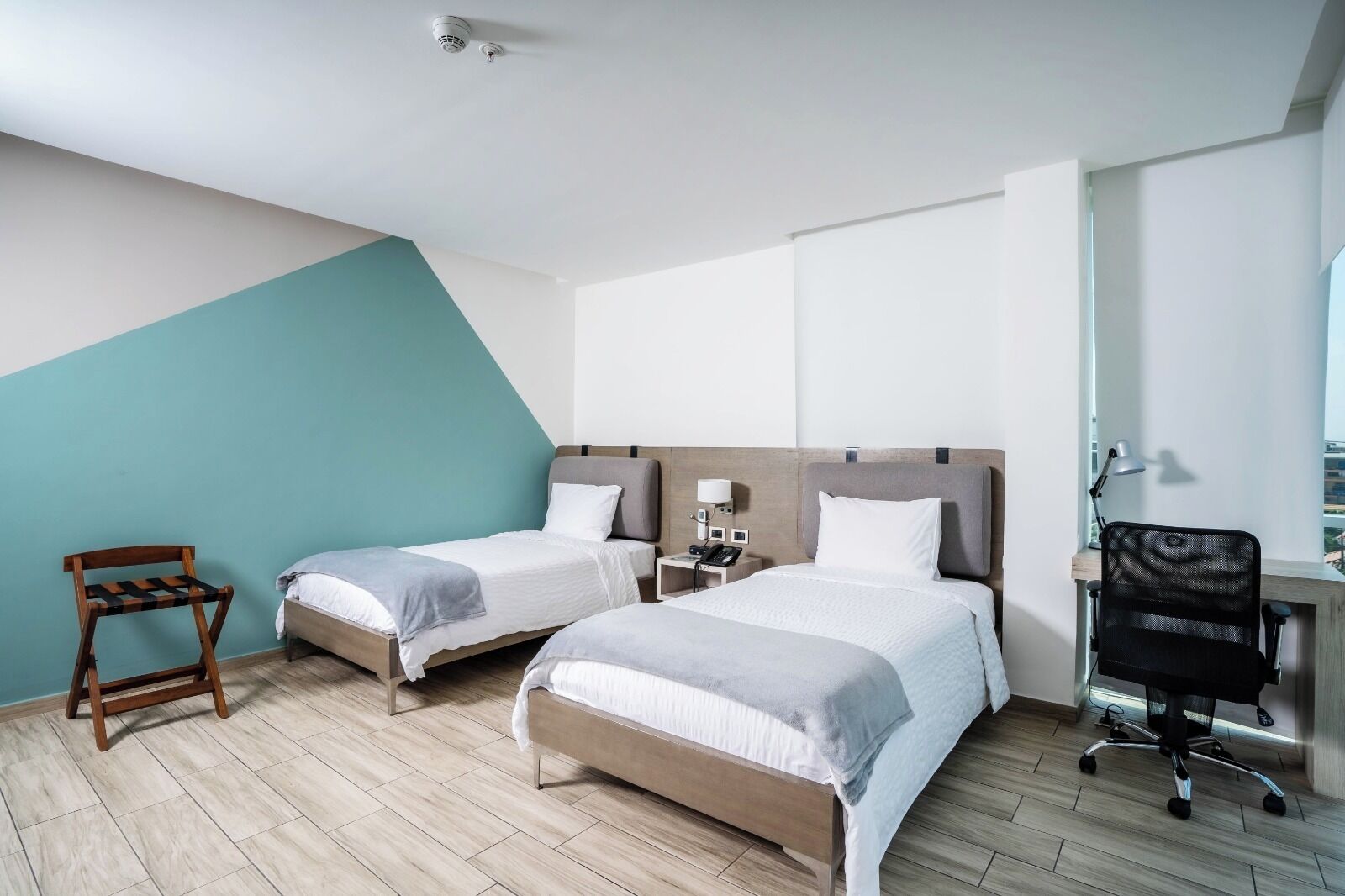 A hotel room with two beds, a desk, a chair, and a small table.