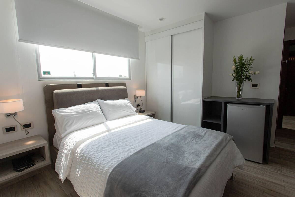 Una habitació d'hotel moderna amb llit, taulells laterals, escriptori i un petit frigorífic.