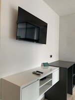 A modern living room with a mounted flat-screen TV, a minimalist white entertainment unit, and a dark-colored sofa.