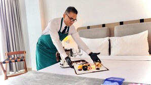 Siisti hotellihuone, jossa on valmiiksi pedattu sänky, yöpöytä, jolla on tarjotinalus täynnä ruokaa, ja tuoli.