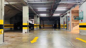 A multi-level underground parking garage with clear directional arrows on the floor, concrete pillars, and a fire extinguisher mounted on a pillar.