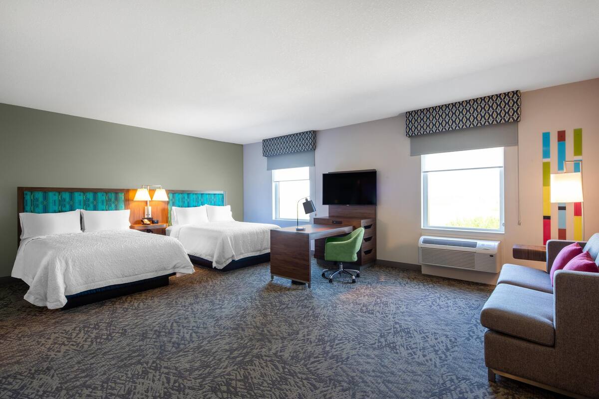 A hotel room with two beds, a desk, a chair, a TV, and a couch.