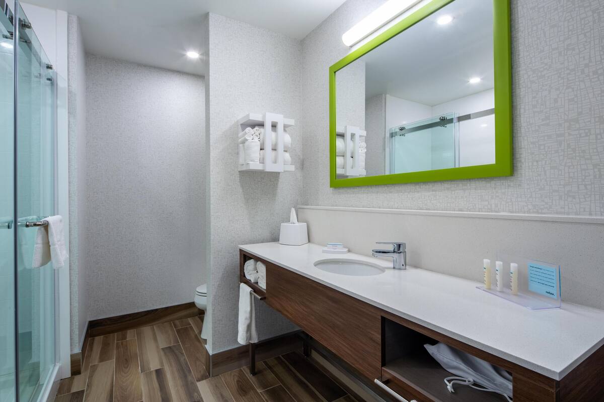 A modern bathroom with a white sink, wooden vanity, and a green-framed mirror.