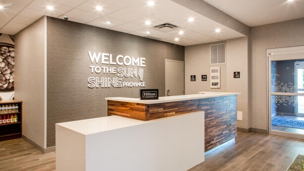 Zona de recepción de hotel con diseño moderno, un mostrador de recepción y un cartel de bienvenida.