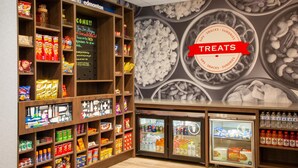 Una sección de aperitivos y dulces con estantes llenos de opciones, un mural en la pared y dos vitrinas refrigeradas.