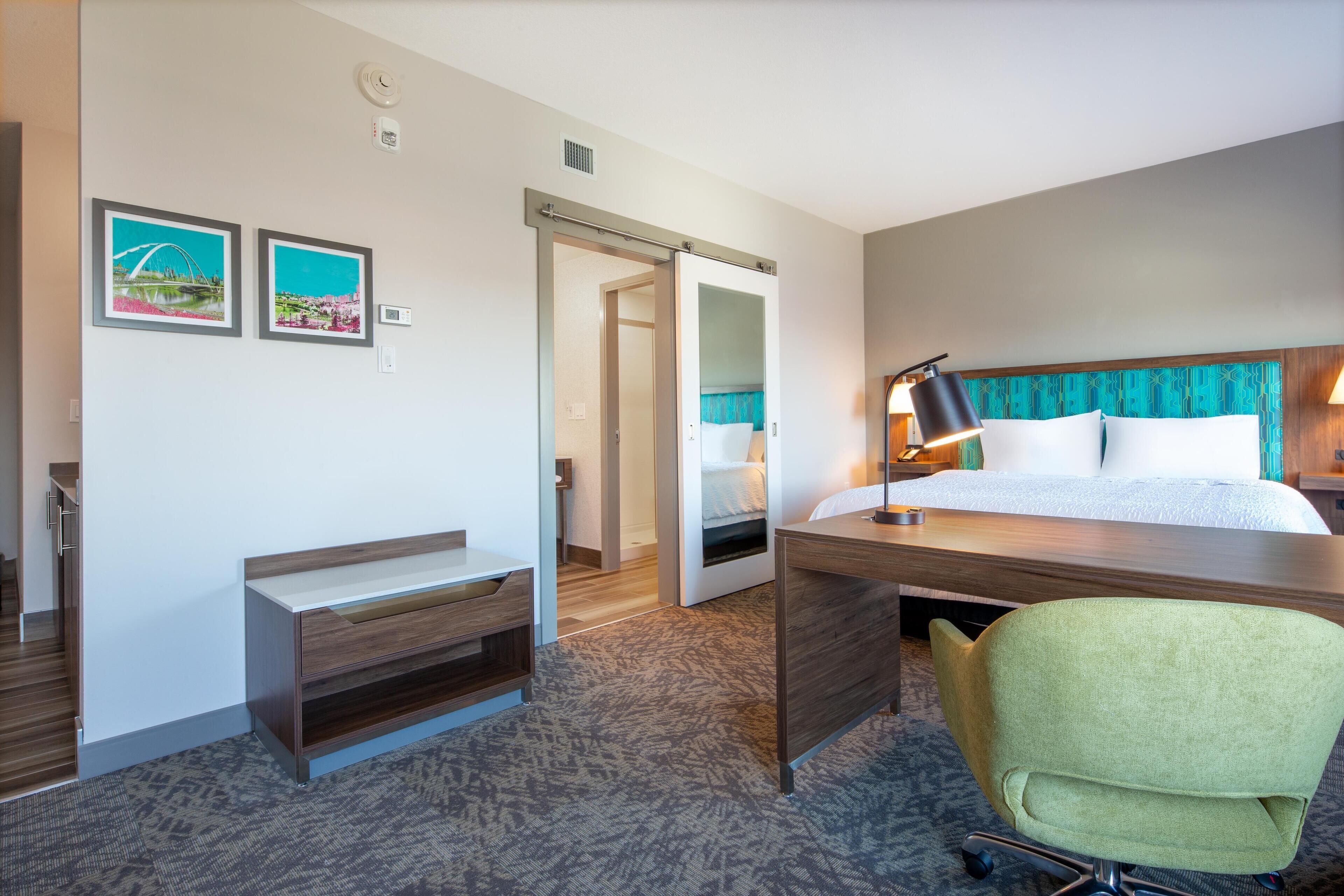 A hotel room with a bed, desk, chair, and a door leading to another room.