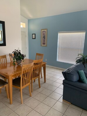 Un coin repas avec une table et des chaises en bois, une plante en pot et une fenêtre avec des stores.