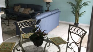 Ein Wohnzimmer mit einem blauen Sofa, zwei Lampen, einem Couchtisch und einer Topfpflanze.