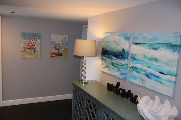 A room with a lamp, a decorative shell, and three paintings on the wall.