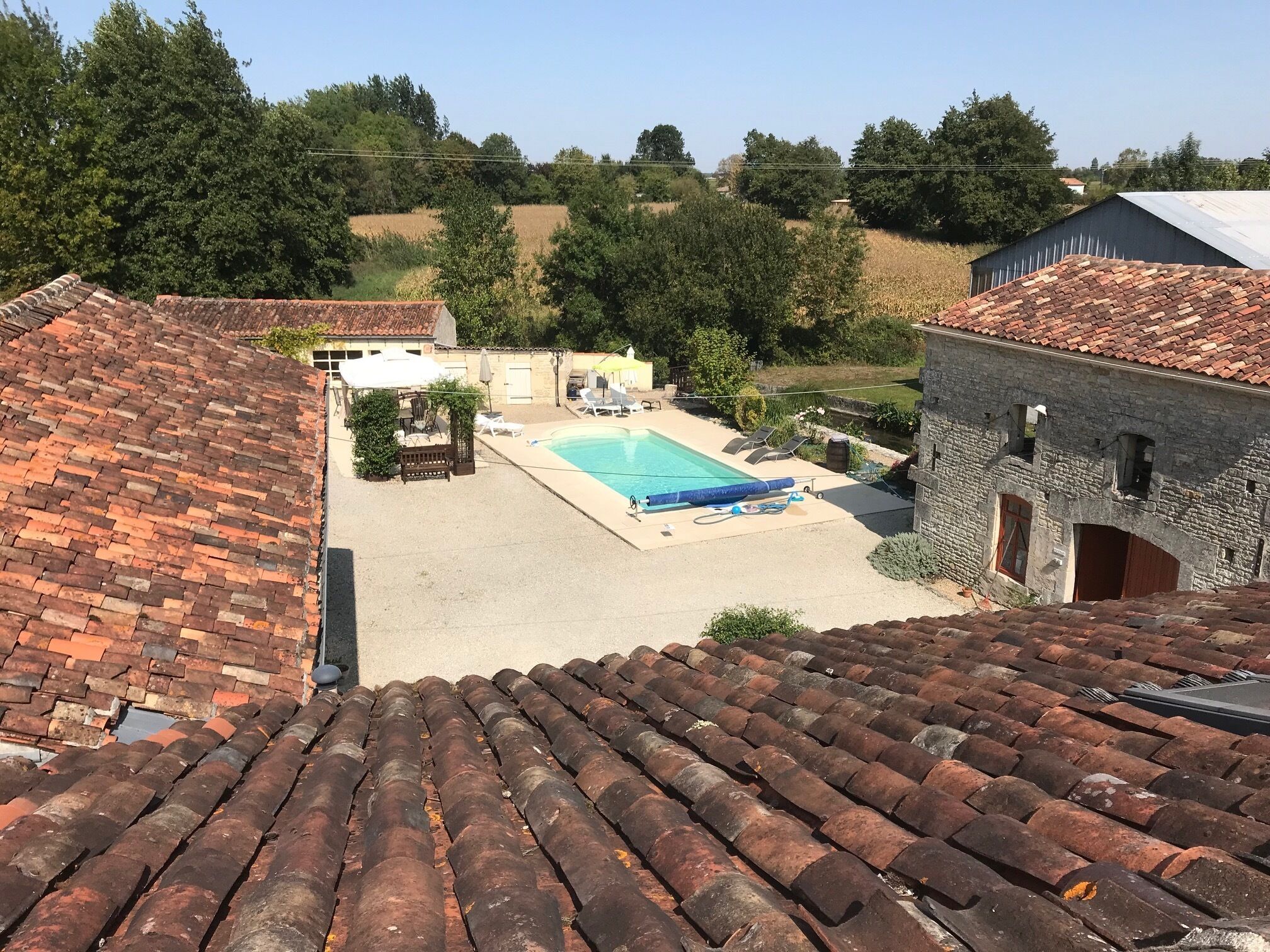 A rooftop view of a property with a swimming pool, a patio area with seating, and a stone building.