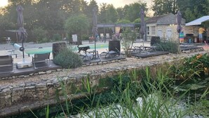 Un espace aménagé au bord de la piscine, avec des chaises longues et des parasols, un petit étang et un mur en pierre.