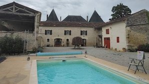 Une cour avec une piscine, un grand bâtiment doté de nombreuses cheminées et un arbre.