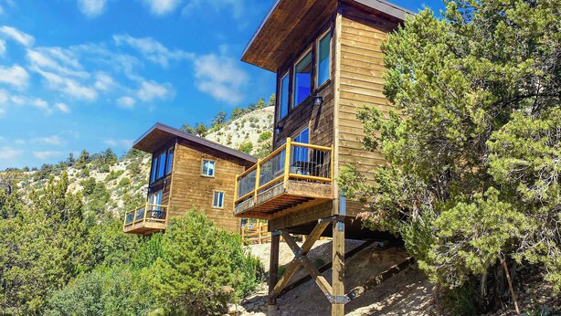 A wooden cabin with a balcony, situated on a hillside with trees. - Romantic Treehouse Retreat near Zion National Park (Orderville)