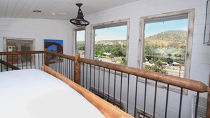 A bedroom with a wooden railing, a bed, and large windows offering a view of a hilly landscape. - Romantic Treehouse Retreat near Zion National Park (Orderville)