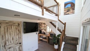 A spacious interior with a wooden staircase, a flat-screen TV, a kitchen area, and a large window. - Romantic Treehouse Retreat near Zion National Park (Orderville)
