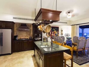 A kitchen with a central island, dark wooden cabinets, a stainless steel sink, and hanging pots.