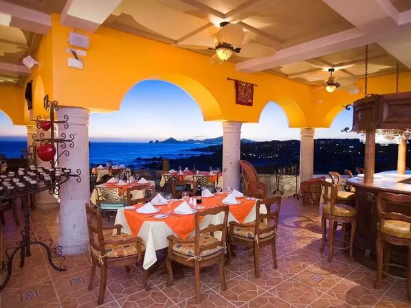 An outdoor dining area with tables set for two, featuring a coastal view.